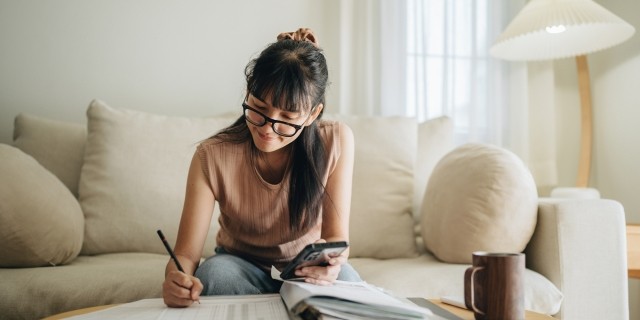 Woman writes in a notebook while sitting on a sofa